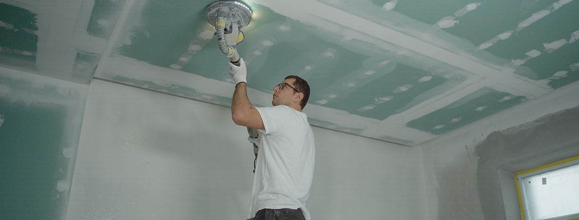 A man in a white shirt painting a ceiling with a roller brush.